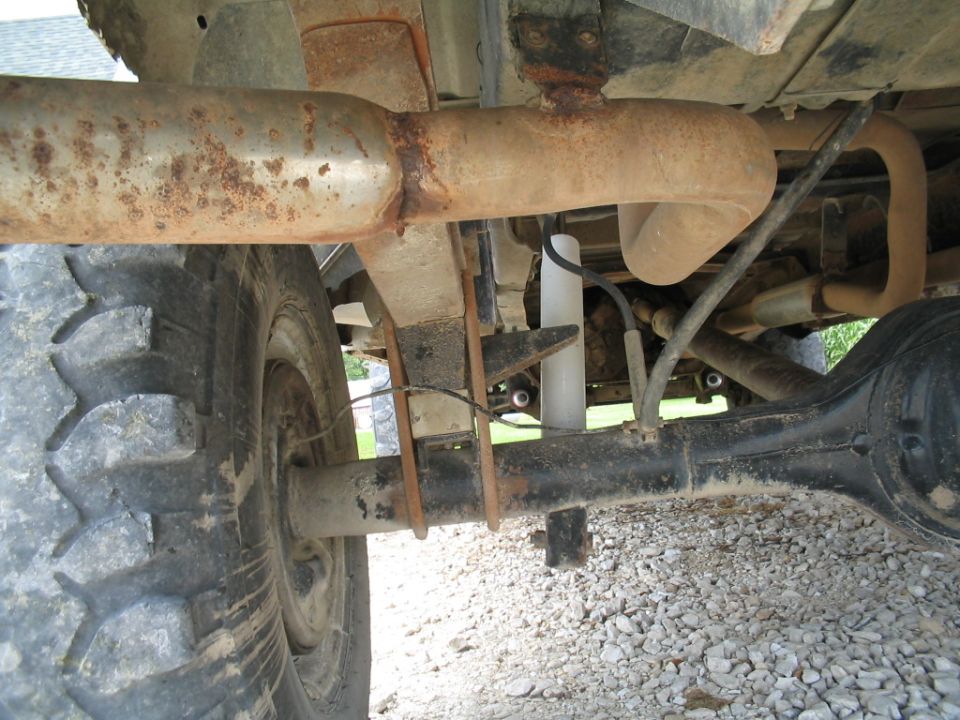 Truck rear axle with leaf springs, shock absorber, and exhaust pipe. Tires are visible