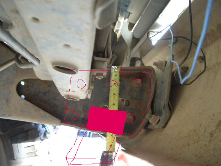 Measuring a bracket on a vehicle's frame with a tape measure