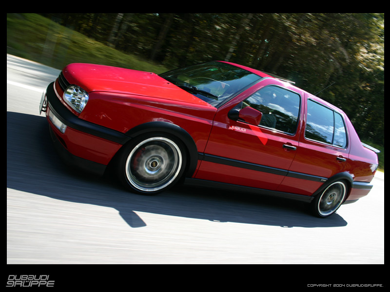 Red sedan driving, 3/4 front view. Appears to be a 1993 Volkswagen Jetta