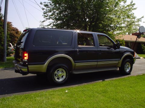 2000 Ford Excursion - A dark blue and tan 2000 Ford Excursion is parked on a paved driveway with a grassy lawn in the foreground.