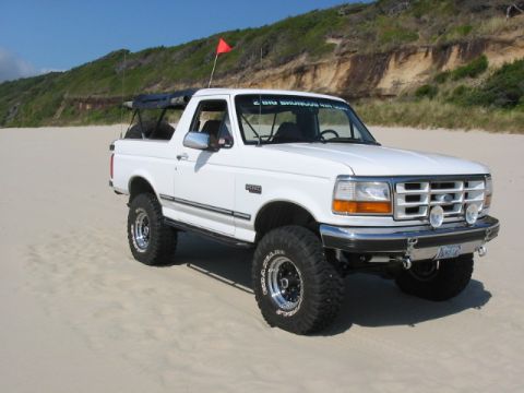 1995 Ford Bronco - This white 1995 Ford Bronco is equipped with off-road tires and parked on a sandy beach, flying a red flag.