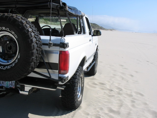 White lifted Ford Bronco with large mud tires and spare tire on a beach