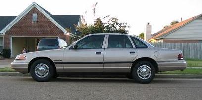 1995 Ford Crown Victoria - A silver 1995 Ford Crown Victoria is parked on the street in front of a house.