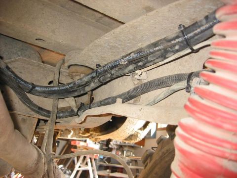 1985 Ford Bronco - Close-up of the undercarriage showing fuel lines and various hoses secured with zip ties.
