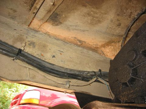 1985 Ford Bronco - The underside of a red vehicle reveals its fuel lines and frame components.