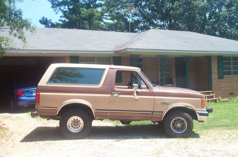 1987 Ford Bronco - A two-tone 1987 Ford Bronco is parked outside a house with a blue car in the garage.