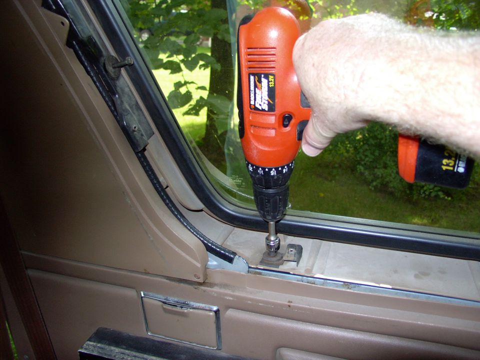 Cordless drill driving a screw into a tan vehicle door frame