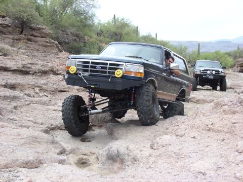 1993 Ford Bronco - A heavily modified Ford Bronco navigates a rocky off-road trail, followed by another vehicle.