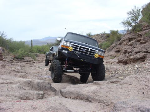 1993 Ford Bronco - A modified black Ford Bronco tackles a challenging rocky trail with another vehicle following behind.