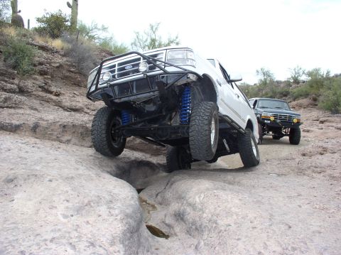 1993 Ford Bronco - Two modified Ford Broncos tackle a challenging rocky trail in a desert landscape.