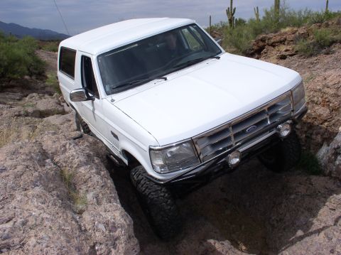 1993 Ford Bronco - A white 1992 Ford Bronco tackles a challenging rocky terrain, demonstrating its off-road capabilities.
