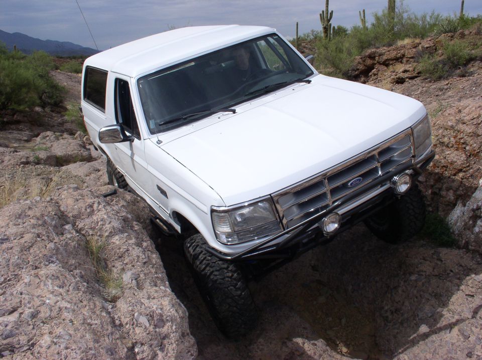 White 1992 Ford Bronco navigating a rocky, off-road trail with saguaro cacti in the background