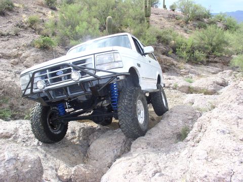 1993 Ford Bronco - This modified SUV tackles a challenging rocky trail, its off-road capabilities with a custom bumper and lifted suspension.