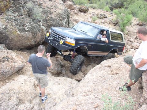 1993 Ford Bronco - A modified Ford Bronco attempts to traverse a challenging rocky trail with onlookers present.