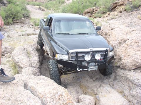 1993 Ford Bronco - A black pickup truck is shown navigating a challenging rocky terrain, with a person standing nearby.