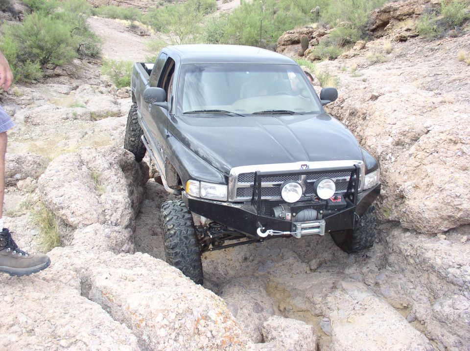 Black pickup truck with off-road tires and bumper navigating a rocky trail