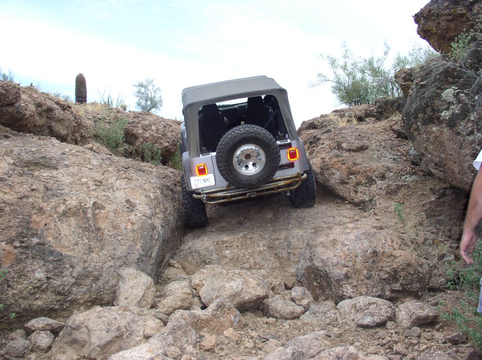 Gray Jeep Wrangler TJ off-roading on a rocky trail, rear view