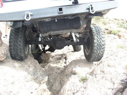 1993 Ford Bronco - The underside of a vehicle is shown as it maneuvers over rough, rocky ground, highlighting its suspension and rear axle.