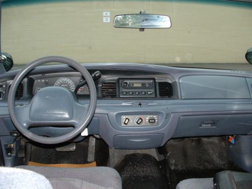 Gray Ford sedan dashboard and steering wheel, center radio and HVAC dials, column shift