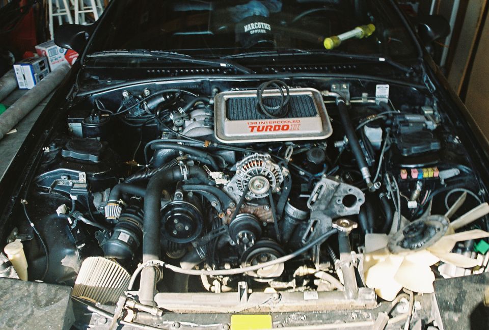 Engine bay of black Mazda RX-7 showing 13B Turbo II engine with intercooler, radiator and fan removed