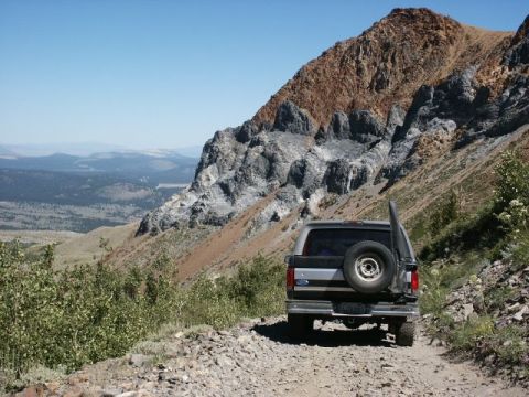1996 Ford Bronco - A gray 1996 Ford Bronco navigates a rocky mountain trail under a clear blue sky.
