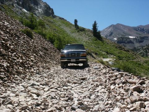 1996 Ford Bronco - Ford Bronco navigates a challenging, rocky mountain trail under a bright blue sky.