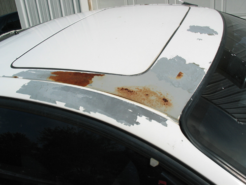 White car roof with peeling paint and rust spots around the sunroof and edges