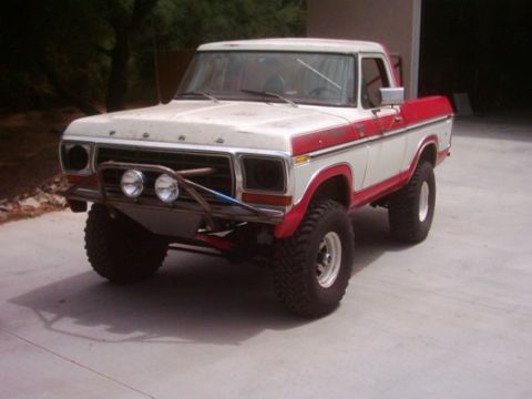 1978 Ford Bronco - Three-quarter front view of a lifted red-and-white late-1970s Ford 4x4 with the top removed, parked on a concrete driveway. It wears a tubu…