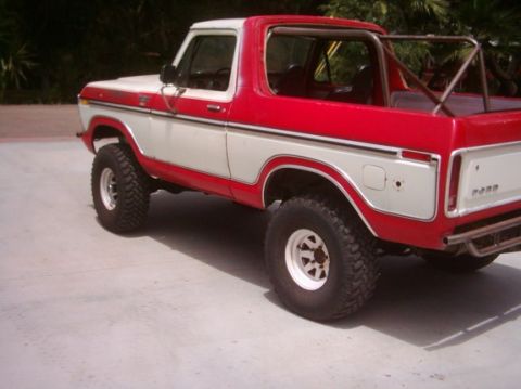 1978 Ford Bronco - Red and white two-tone full-size Ford Bronco viewed from the rear three-quarter side on a concrete driveway, with the hardtop removed to ex…