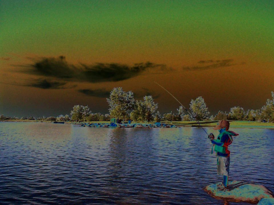 Person fishing from rocks at a lake under a surreal green-orange sky