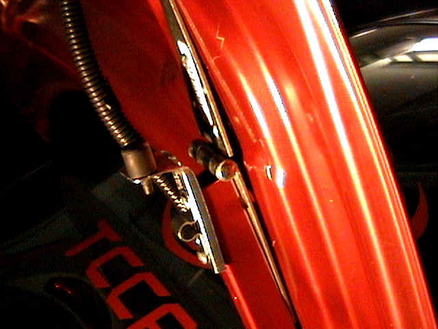 Close-up of glossy red panel with chrome trim, bolts and a braided hose