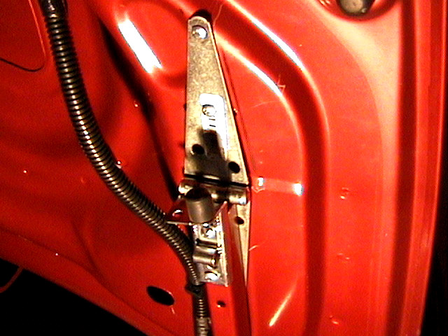 Metal hinge and black wiring conduit mounted inside a red car body panel