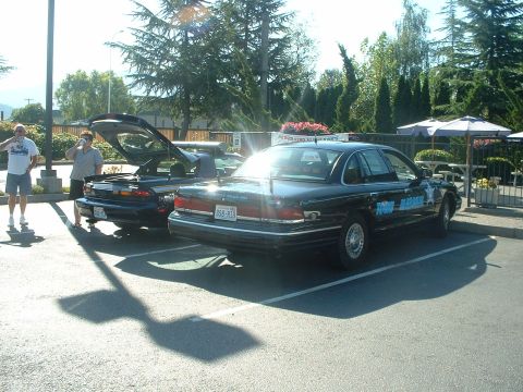 1999 Ford Crown Victoria - A police car is parked in a lot next to another vehicle with its trunk open.
