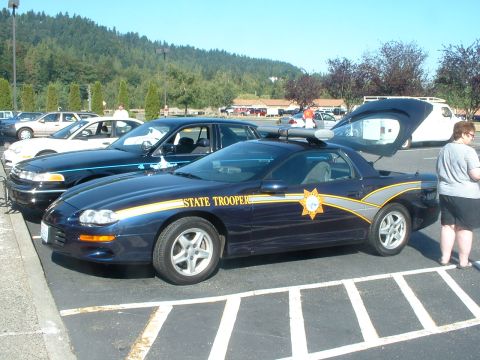 1999 Ford Crown Victoria - A dark blue police car, possibly a Chevrolet Camaro, is parked next to other vehicles.
