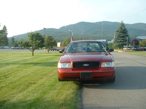 1999 Ford Crown Victoria - Front view of a red Ford Crown Victoria parked on a grassy area next to a paved road.