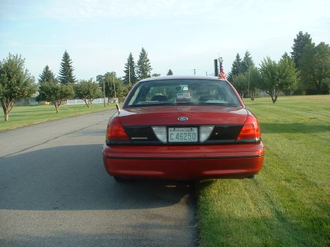 1999 Ford Crown Victoria - This red Ford Crown Victoria has a Washington state license plate and an American flag on the antenna.