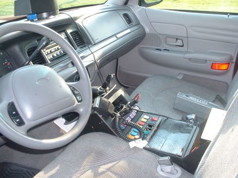 1999 Ford Crown Victoria - The interior of a police vehicle is shown, equipped with a radio console and other communication devices.