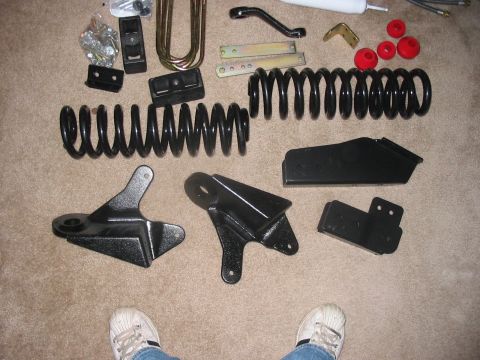 1988 Ford Bronco - Various suspension lift kit parts are laid out on a carpeted floor, including springs, U-bolts, and mounting brackets.
