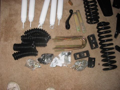 1988 Ford Bronco - Various vehicle lift kit components are laid out on a carpeted floor, including shocks, springs, and hardware.