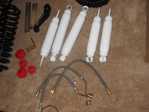 1988 Ford Bronco - Collection of suspension components, including shocks, springs, and brake lines, laid out on a carpeted surface.