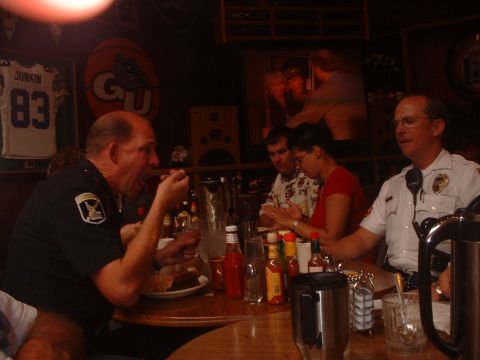 1999 Ford Crown Victoria - Two officers and civilians dine together at a table in a restaurant, with sports memorabilia visible on the wall.
