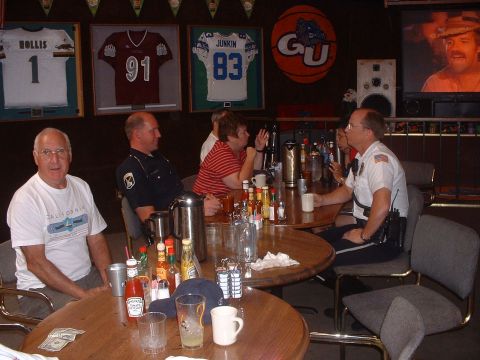 1999 Ford Crown Victoria - A group of people, including two in uniform, are seated at tables in a bar decorated with sports memorabilia and a television screen.