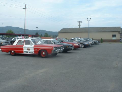 1999 Ford Crown Victoria - A line of vehicles including a vintage fire department car is parked in a lot.
