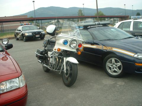 1999 Ford Crown Victoria - A police motorcycle is parked next to a State Trooper car, with another police car in the background.