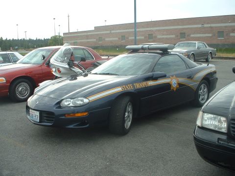 1999 Ford Crown Victoria - A Chevrolet Camaro serves as a state trooper vehicle, parked alongside other cars.