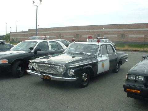 1999 Ford Crown Victoria - Two police cars, one vintage and one modern, parked outdoors in front of a brick building.