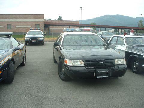 1999 Ford Crown Victoria - A black police car, possibly a Ford Crown Victoria, is parked in front of a building with other police vehicles visible.
