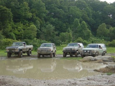 1994 Ford Bronco - Several off-road vehicles are lined up next to a large puddle in a wooded area.