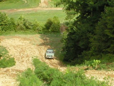 1994 Ford Bronco - An off-road vehicle navigates a dusty trail surrounded by greenery.