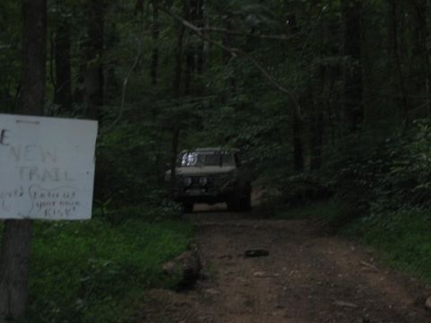 1994 Ford Bronco - A vehicle is parked on a dirt path in a wooded area next to a sign warning of a new trail.